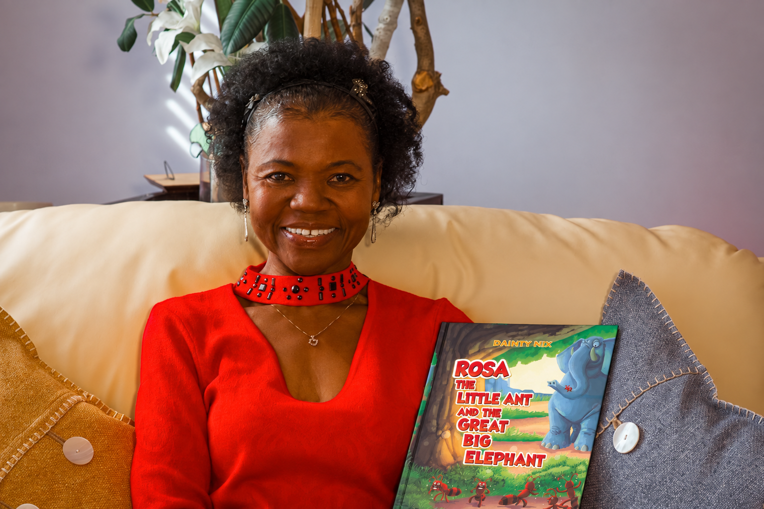 Dainty Nix seated on a sofa holding the updated cover of Rosa the Little Ant and the Great Big Elephant